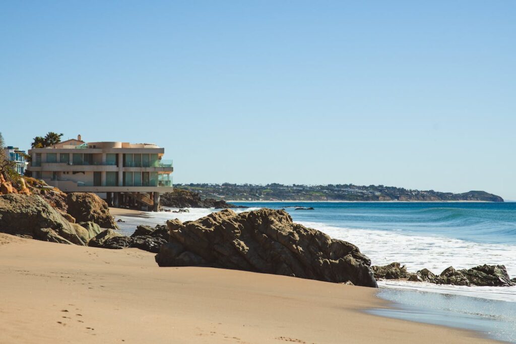 Stylish beach house overlooking the ocean, surrounded by rocks and sandy shores.