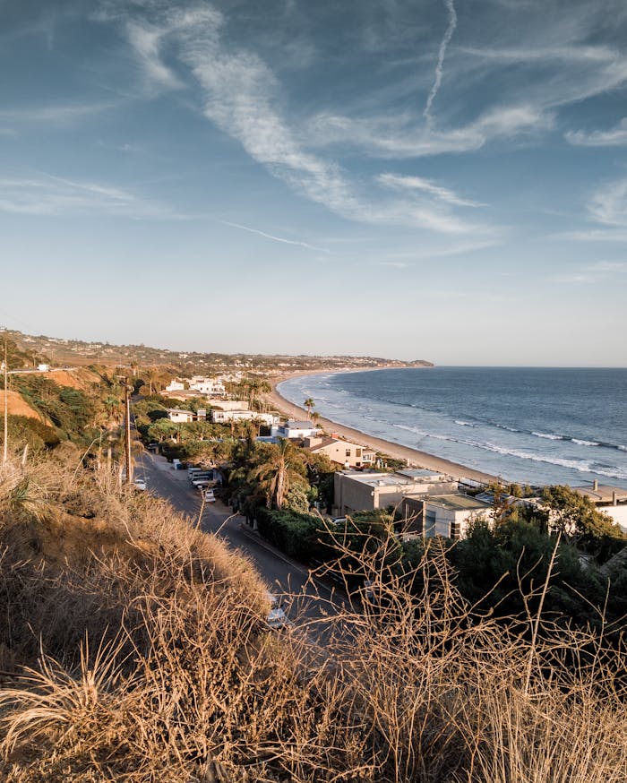 Aerial view of Malibu coastline with ocean, beach, and residential area under a clear sky.